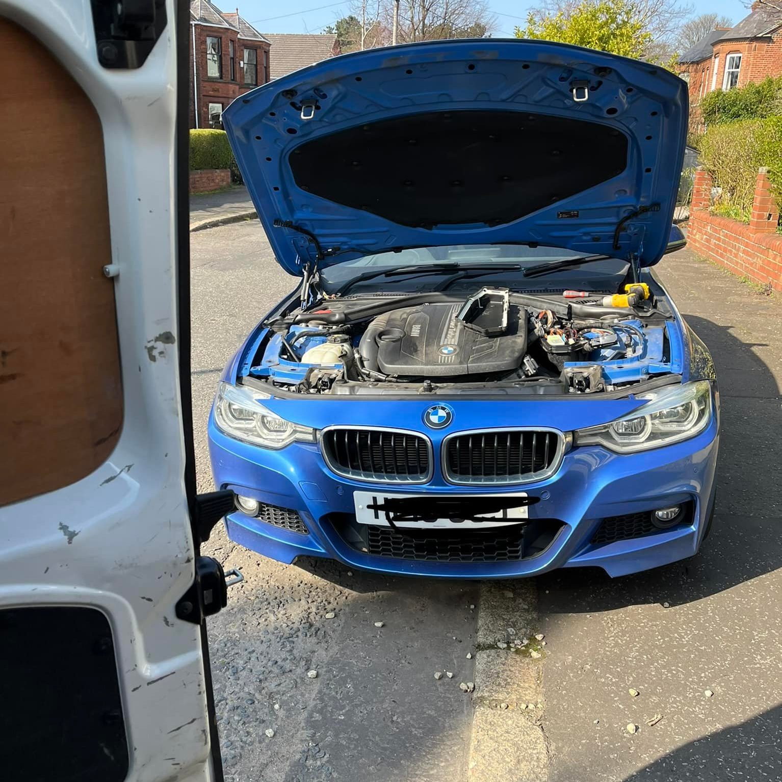 Blue BMW parked on a curb with the bonnet opened